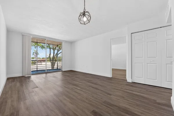 a view of an empty room with wooden floor and fan