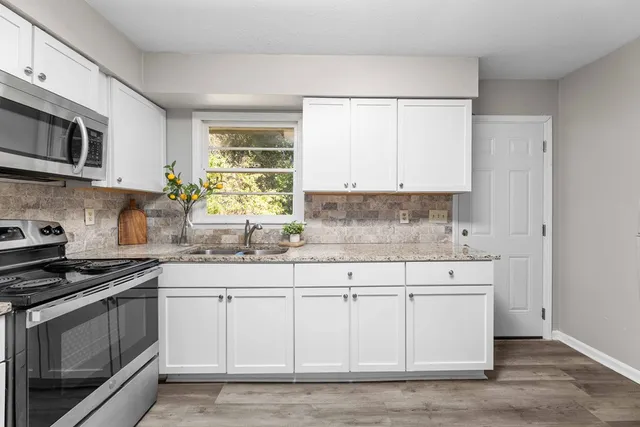 a kitchen with stainless steel appliances granite countertop white cabinets a sink and a stove