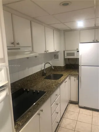 a kitchen with granite countertop white cabinets and refrigerator