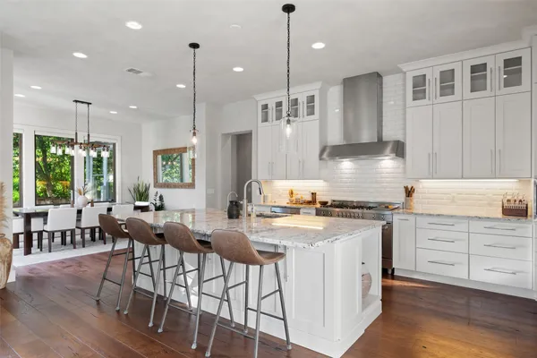 a kitchen with stainless steel appliances granite countertop a stove a sink dishwasher a refrigerator and white cabinets with wooden floor