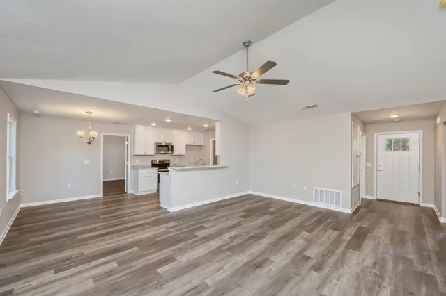 a view of an empty room and kitchen view with wooden floor