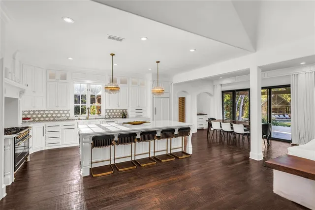 a large dining hall with stainless steel appliances granite countertop a stove a sink a dining table and chairs with wooden floor