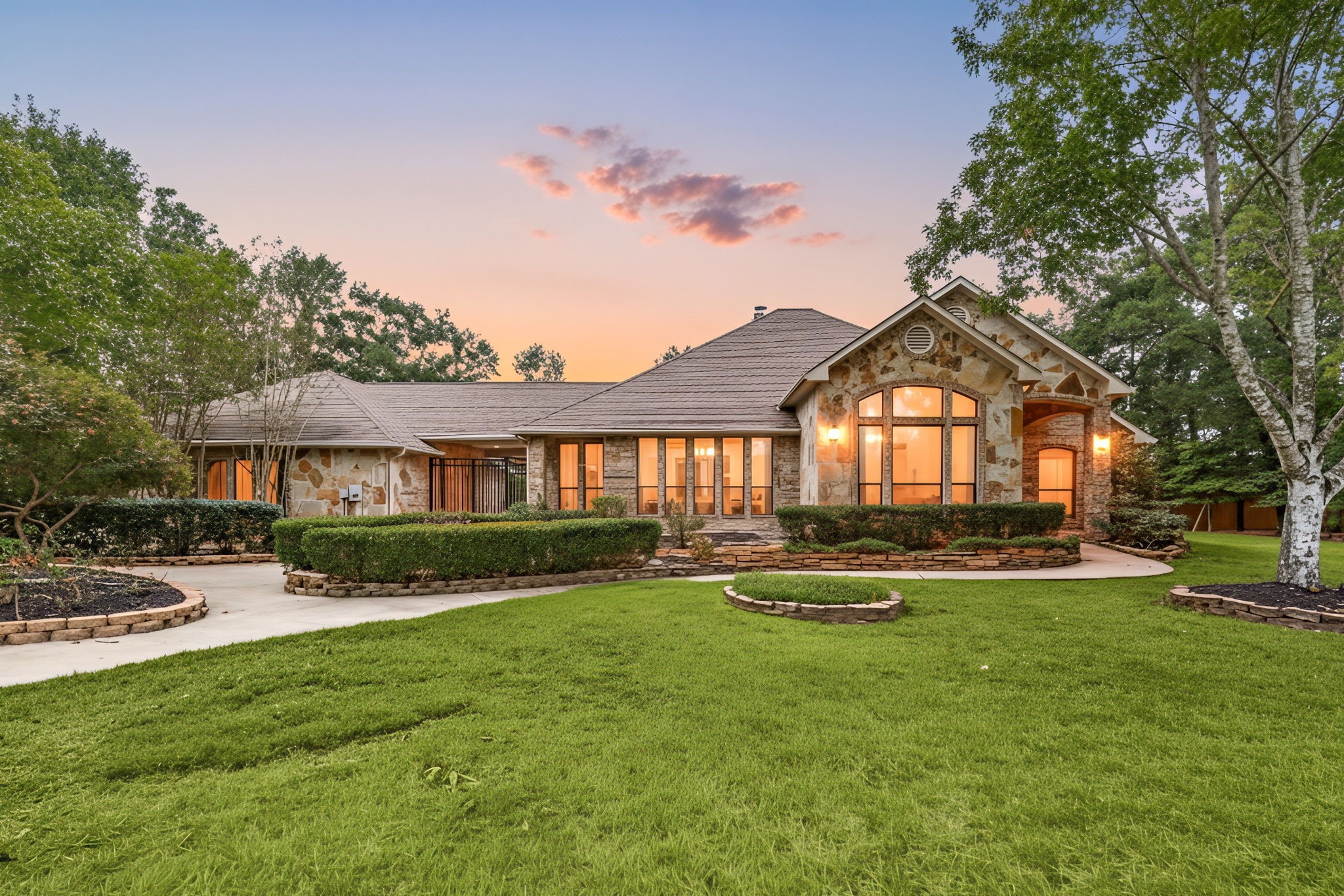 28618 Benders Crossing Drive Spring, TX 77386 - Photo 2 of 46 Striking twilight exterior showcasing the home’s stone façade, architectural windows, and warm interior lighting. Lush landscaping and mature trees frame this inviting estate, creating an unforgettable first impression.