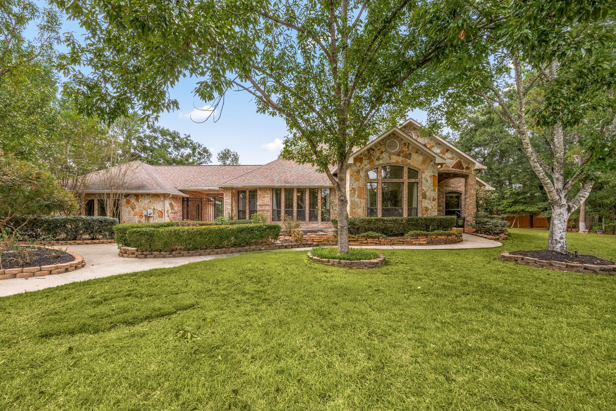 28618 Benders Crossing Drive Spring, TX 77386 - Photo 3 of 46 Beautiful daytime view highlighting the home’s expansive single-story layout, natural stone and brick exterior, and meticulously maintained lawn. Mature shade trees and curved walkways enhance curb appeal and functionality.