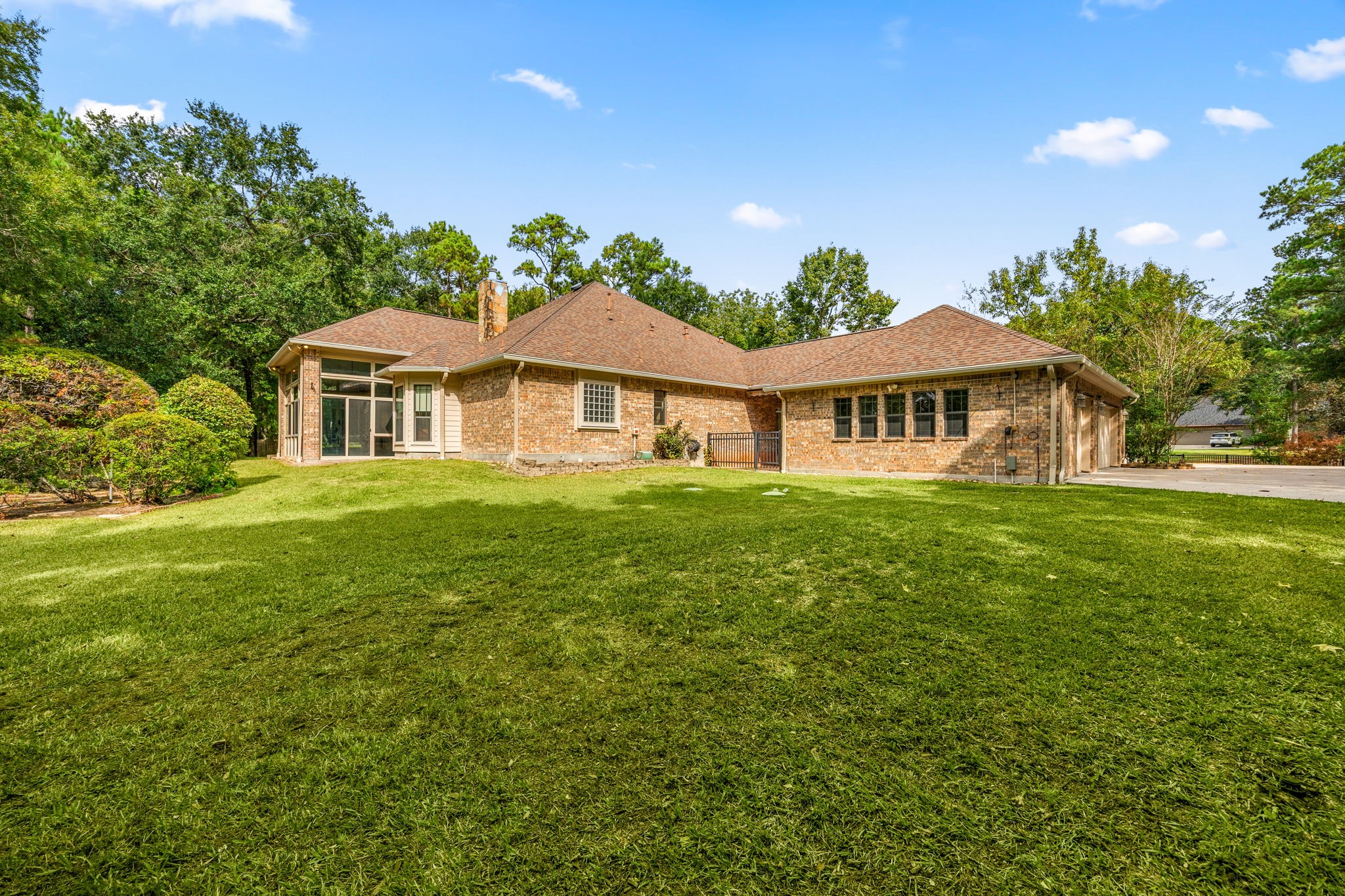 28618 Benders Crossing Drive Spring, TX 77386 - Photo 38 of 46 Wide rear exterior view showcasing the home’s brick construction, enclosed sunroom, and expansive lawn, all set against a backdrop of mature trees and established landscaping.
