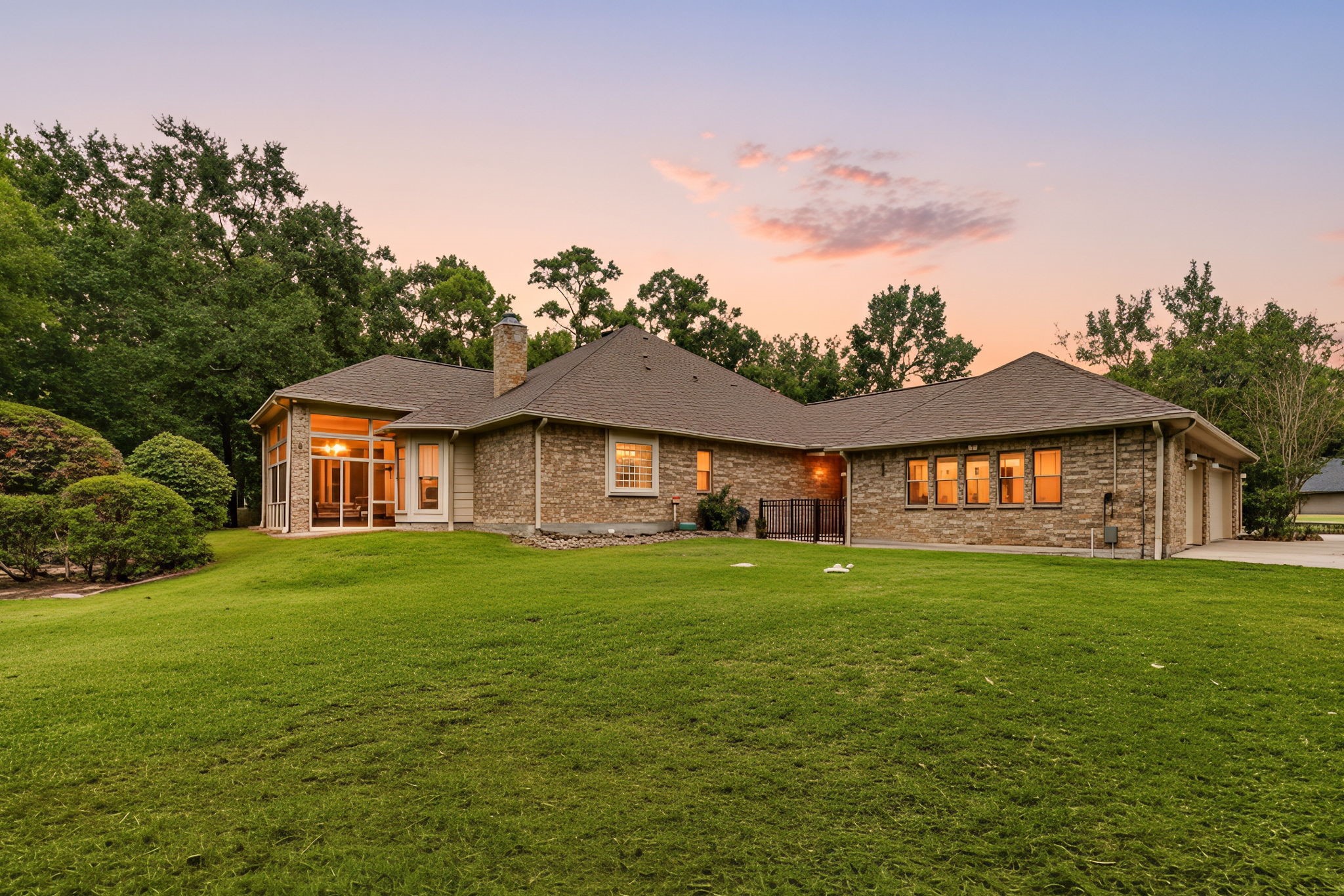 28618 Benders Crossing Drive Spring, TX 77386 - Photo 39 of 46 Rear exterior view showcasing the home’s timeless brick façade, expansive backyard, and enclosed sunroom, all framed by mature trees. Warm interior lighting highlights the home’s inviting evening presence.