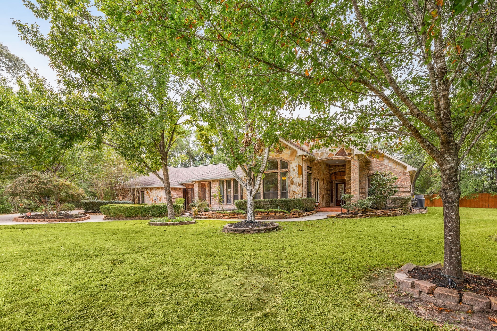 28618 Benders Crossing Drive Spring, TX 77386 - Photo 4 of 46 Charming daytime view highlighting the home’s stone and brick exterior, graceful arched entry, and beautifully landscaped front yard. Mature shade trees, manicured lawn, and curved walkways create a serene setting and enhance the home’s timeless curb appeal.