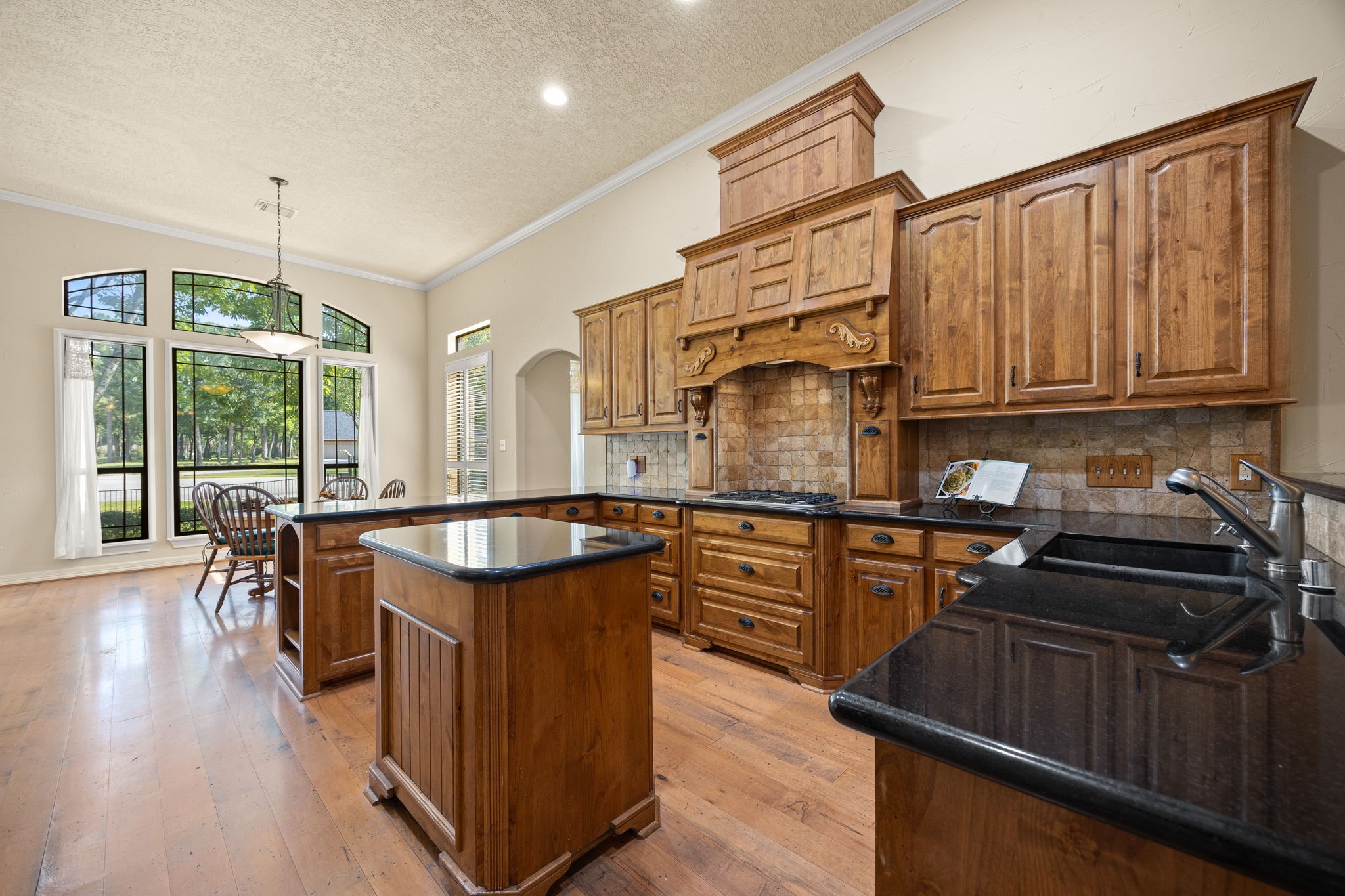 28618 Benders Crossing Drive Spring, TX 77386 - Photo 8 of 46 Spacious gourmet kitchen featuring custom wood cabinetry, a decorative wood vent hood, granite countertops, and center island with additional prep space. Open sightlines to the breakfast area and large windows bring in abundant natural light, creating an ideal space for everyday living and entertaining.