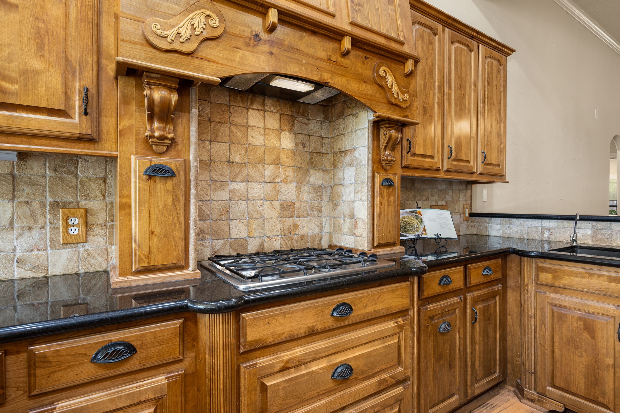 28618 Benders Crossing Drive Spring, TX 77386 - Photo 10 of 46 Detailed view of the kitchen’s custom wood vent hood, gas cooktop, and stone tile backsplash. Rich wood cabinetry and granite countertops highlight the craftsmanship and timeless design of this well-appointed cooking space.