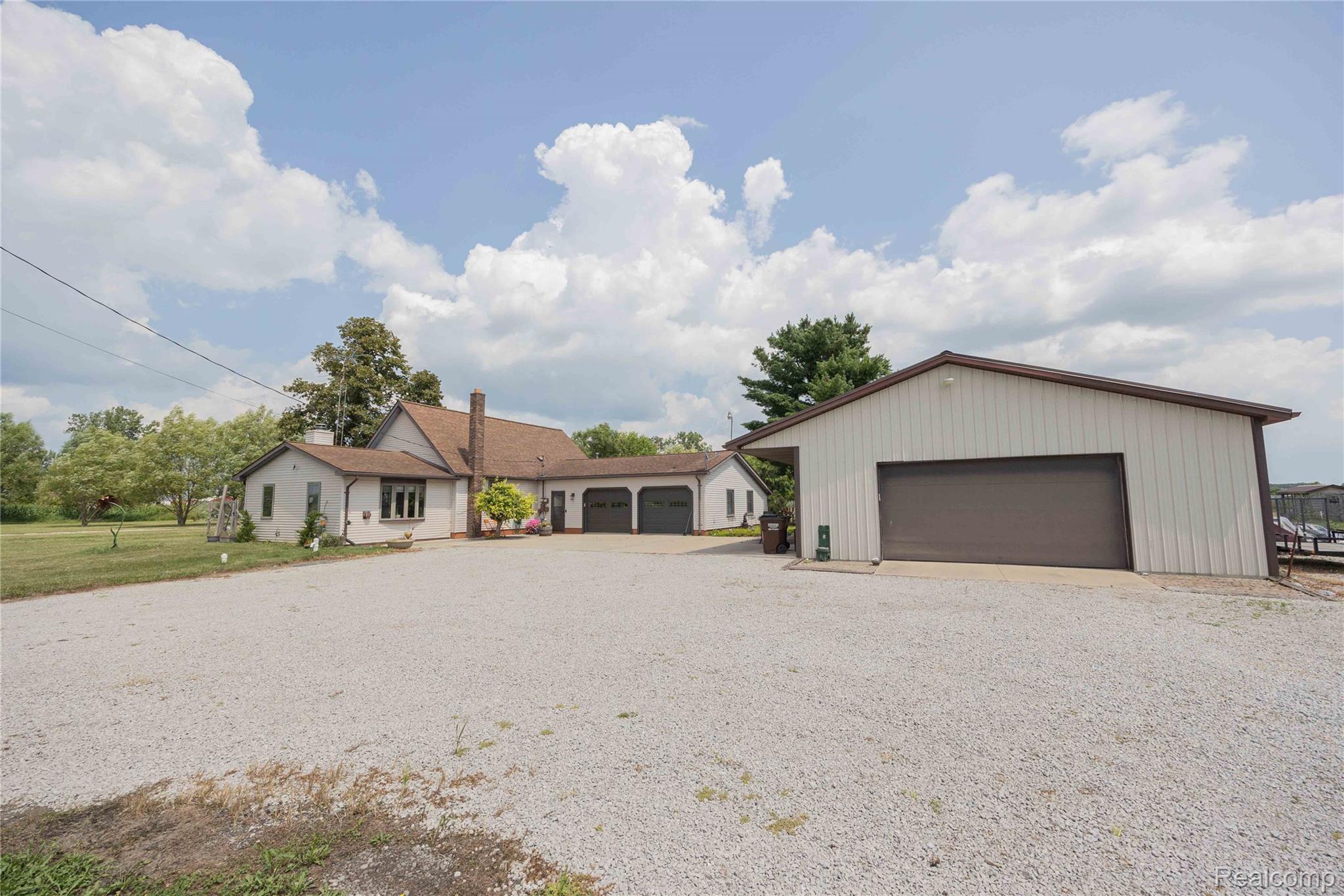 9160 Steffas Road Maybee, MI 48159 - Photo 2 of 36 Expansive gravel parking area, two-car attached garage, additional detached garage, and a brick chimney accent