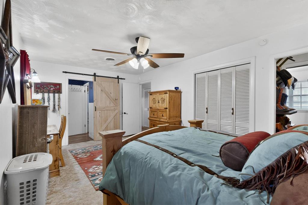 202 Senter Valley Road Irving, TX 75060 - Photo 18 of 32 Bedroom featuring a ceiling fan with light fixture, wood-finish barn door, white louvered bifold closet doors, and light-toned carpeting