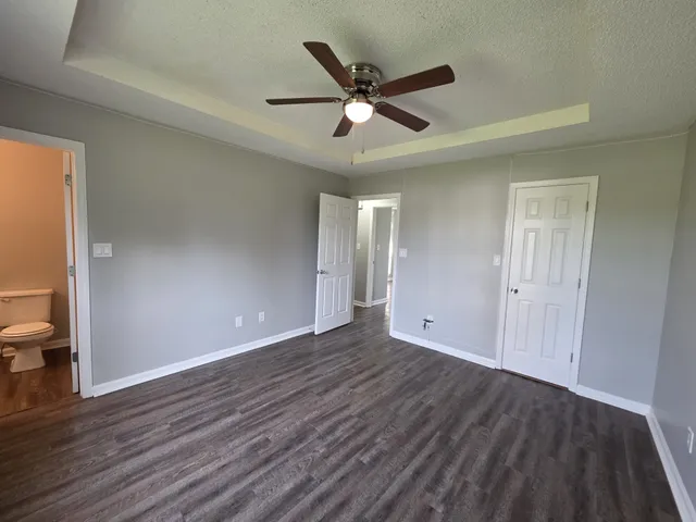 a view of an empty room with wooden floor and a ceiling fan