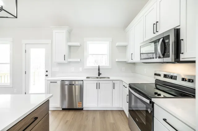 a kitchen with stainless steel appliances white cabinets a sink dishwasher a stove and a refrigerator with wooden floor