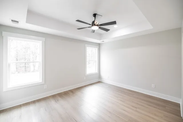 an empty room with wooden floor fan and windows
