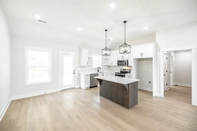 a large kitchen with stainless steel appliances granite countertop a sink a stove a refrigerator and white cabinets with wooden floor