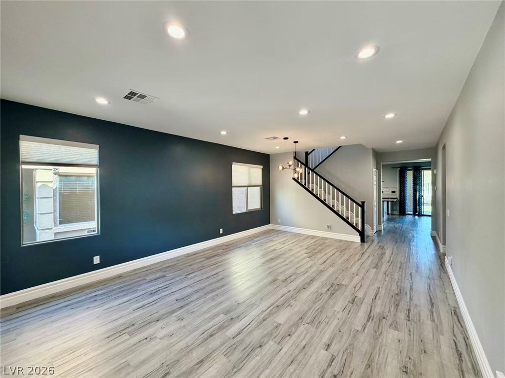 135 Tall Ruff Drive Las Vegas, NV 89148 - Photo 2 of 29 A generous living space featuring light wood-look flooring and a modern chandelier illuminating the staircase.
