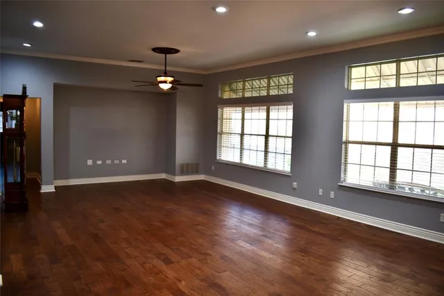 an empty room with wooden floor ceiling fan and windows