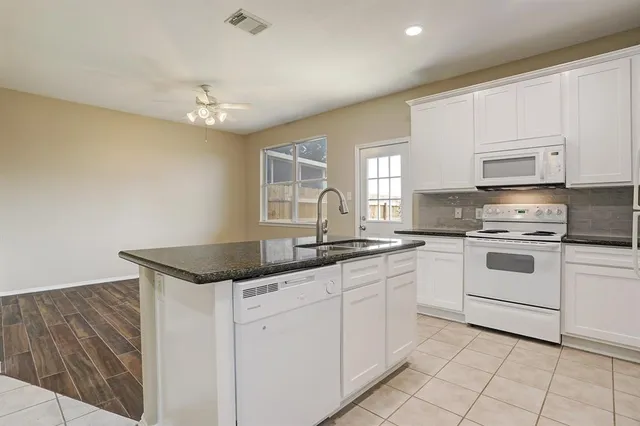 a kitchen with granite countertop white cabinets white appliances a sink and a window
