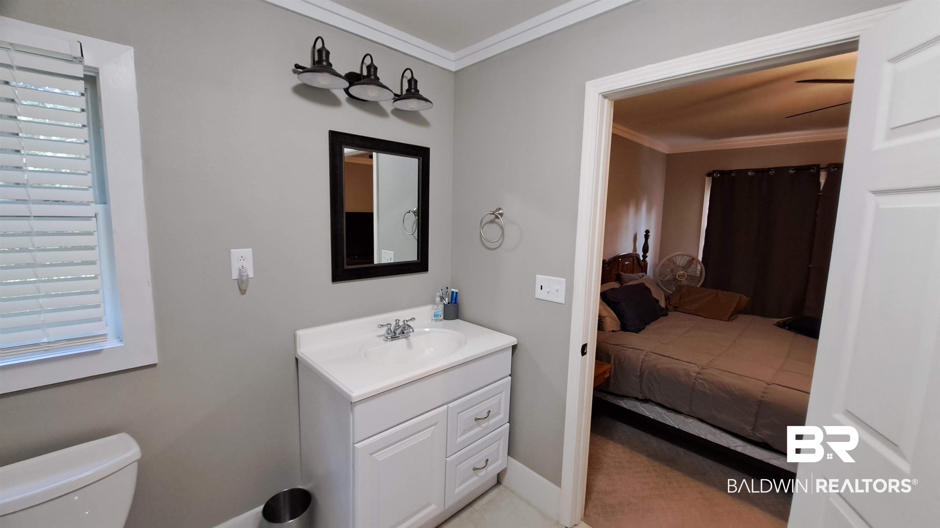 110 South Main Street Evergreen, AL 36401 - Photo 17 of 27 White vanity with an integrated sink and chrome faucet, framed mirror, and a three-light fixture