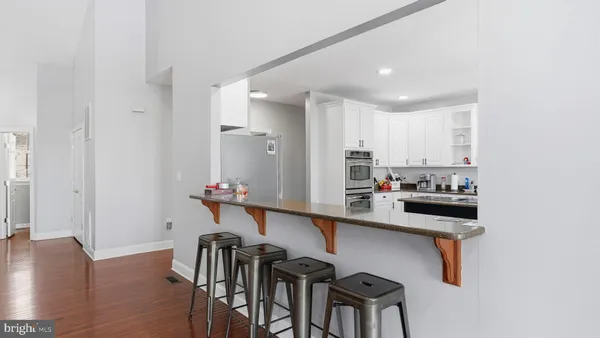 a large white kitchen with granite countertop a stove a sink a refrigerator and white cabinets with wooden floor