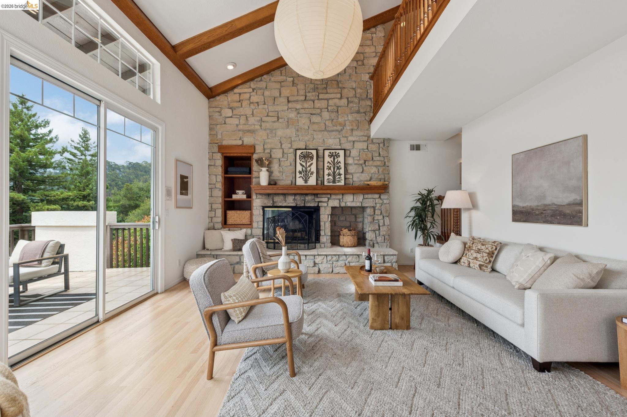 Vaulted ceiling living space featuring a stone fireplace with a wood mantle, an upper-level balcony with wood railing, and wood-finish flooring