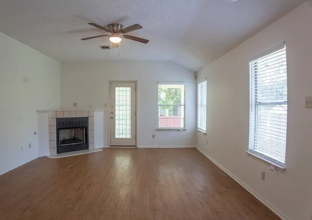 a view of an empty room with wooden floor fireplace and a window