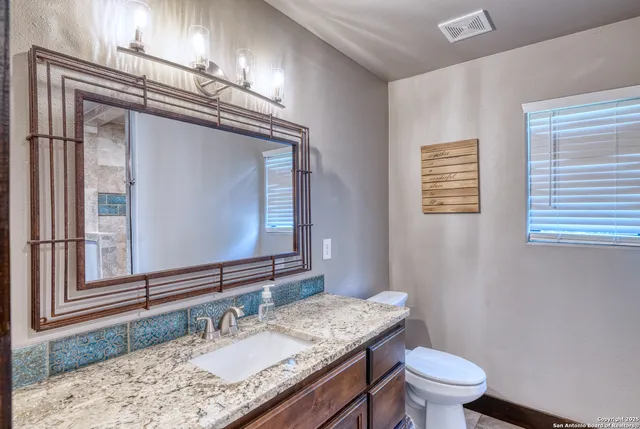 a bathroom with a granite countertop toilet a sink and a mirror