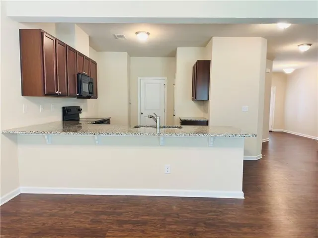 a view of a kitchen with kitchen island a sink wooden floor and black cabinets