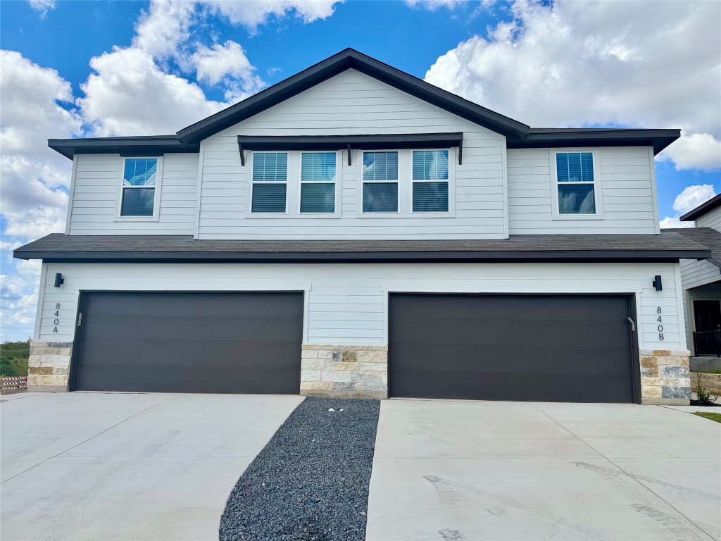 View of front of home featuring stone siding, a garage, driveway, and a shingled roof