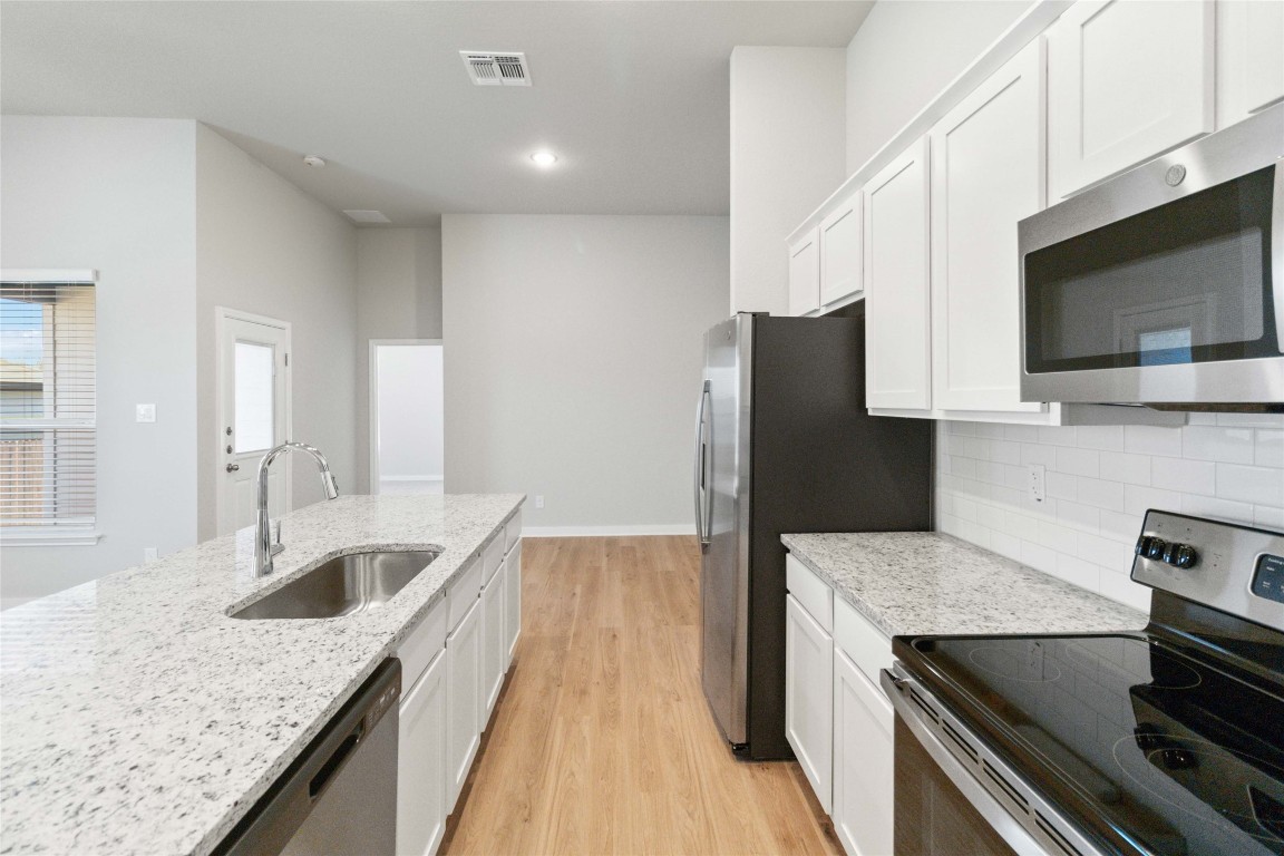 840 Staglin Street, Unit B Buda, TX 78610 - Photo 6 of 17 Kitchen featuring appliances with stainless steel finishes, light stone counters, white cabinets, light wood finished floors, and backsplash