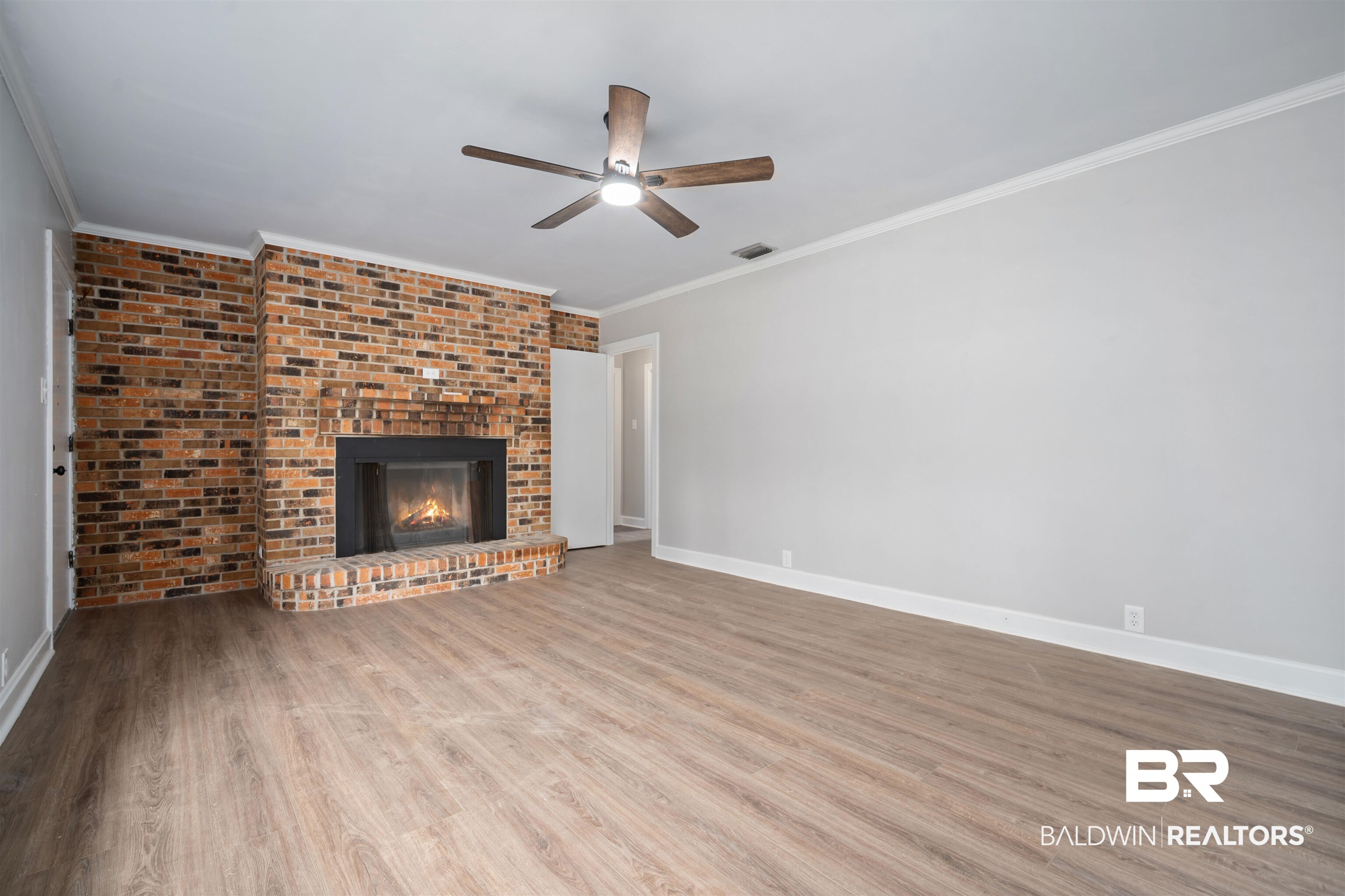 2261 Island Road Mobile, AL 36605 - Photo 5 of 25 Unfurnished living room featuring light wood-style flooring, a fireplace, crown molding, ceiling fan, and brick wall