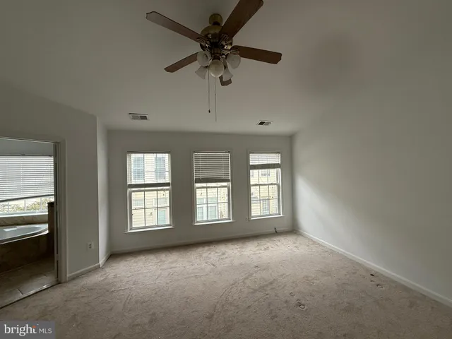 an empty room with chandelier fan and windows