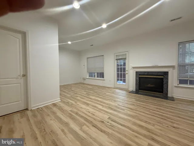 a view of an empty room with wooden floor fireplace and a window
