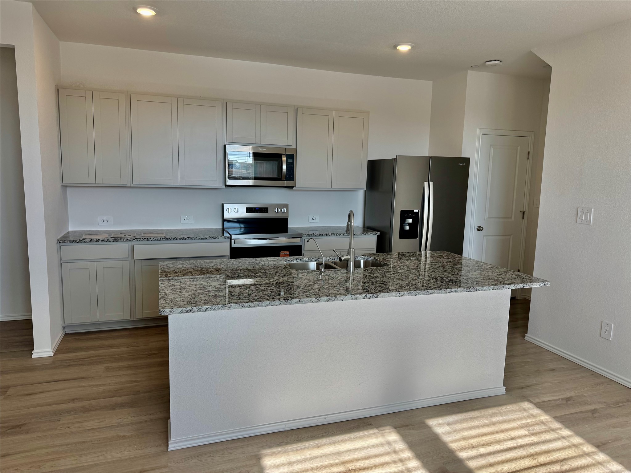 104 Calcite Road Kyle, TX 78640 - Photo 2 of 21 Kitchen with appliances with stainless steel finishes, light wood-style flooring, an island with sink, light stone counters, and recessed lighting
