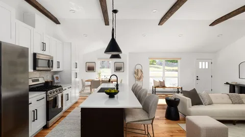 a living room with stainless steel appliances a dining table wooden floor and a window