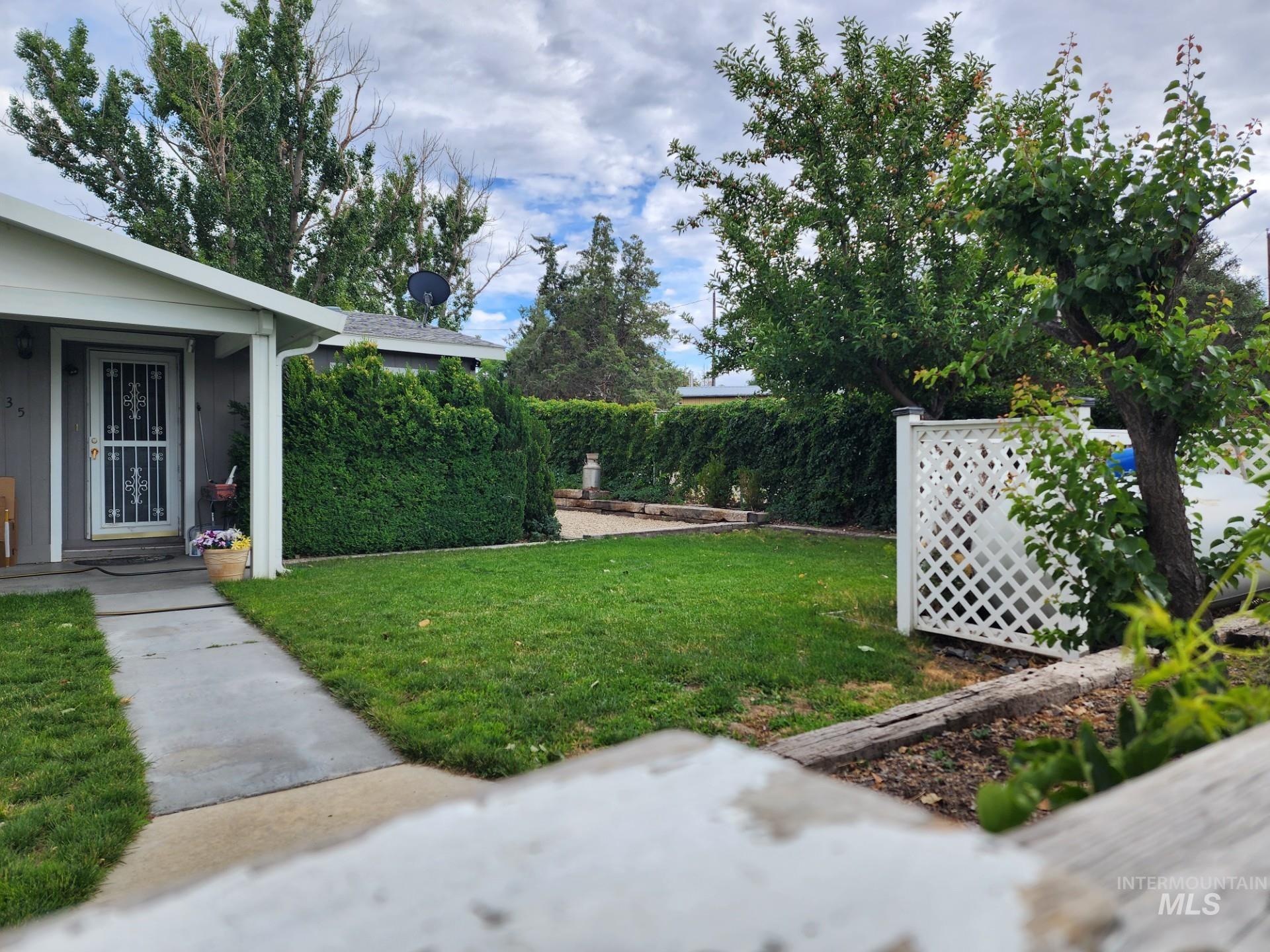 235 5th Street Grand View, ID 83624 - Photo 2 of 22 Front yard featuring a manicured lawn, established shrubs, a concrete pathway, a privacy lattice screen, and mature trees