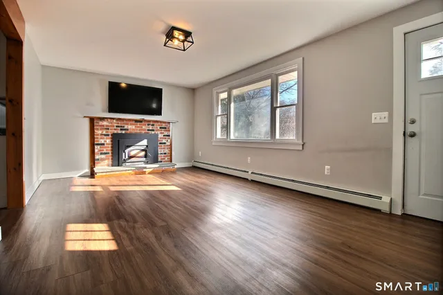 an empty room with wooden floor fireplace and windows