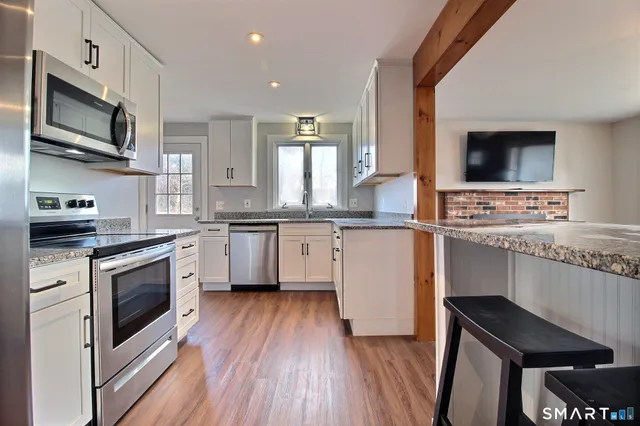 a kitchen with stainless steel appliances white cabinets a sink a stove a microwave and wooden floors