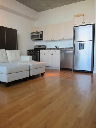 a living room with stainless steel appliances wooden floor and a refrigerator
