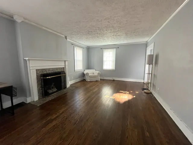 an empty room with wooden floor fireplace and windows