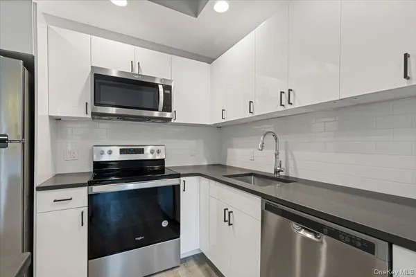 a kitchen with stainless steel appliances granite countertop a stove top oven a sink and white cabinets