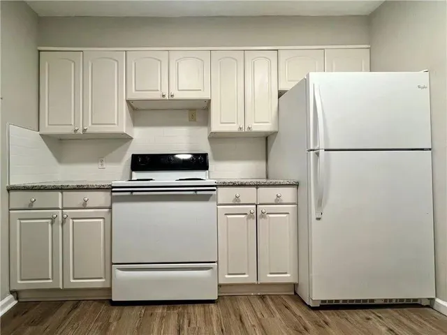 a white refrigerator freezer and a stove sitting inside of a kitchen with granite countertop white cabinets