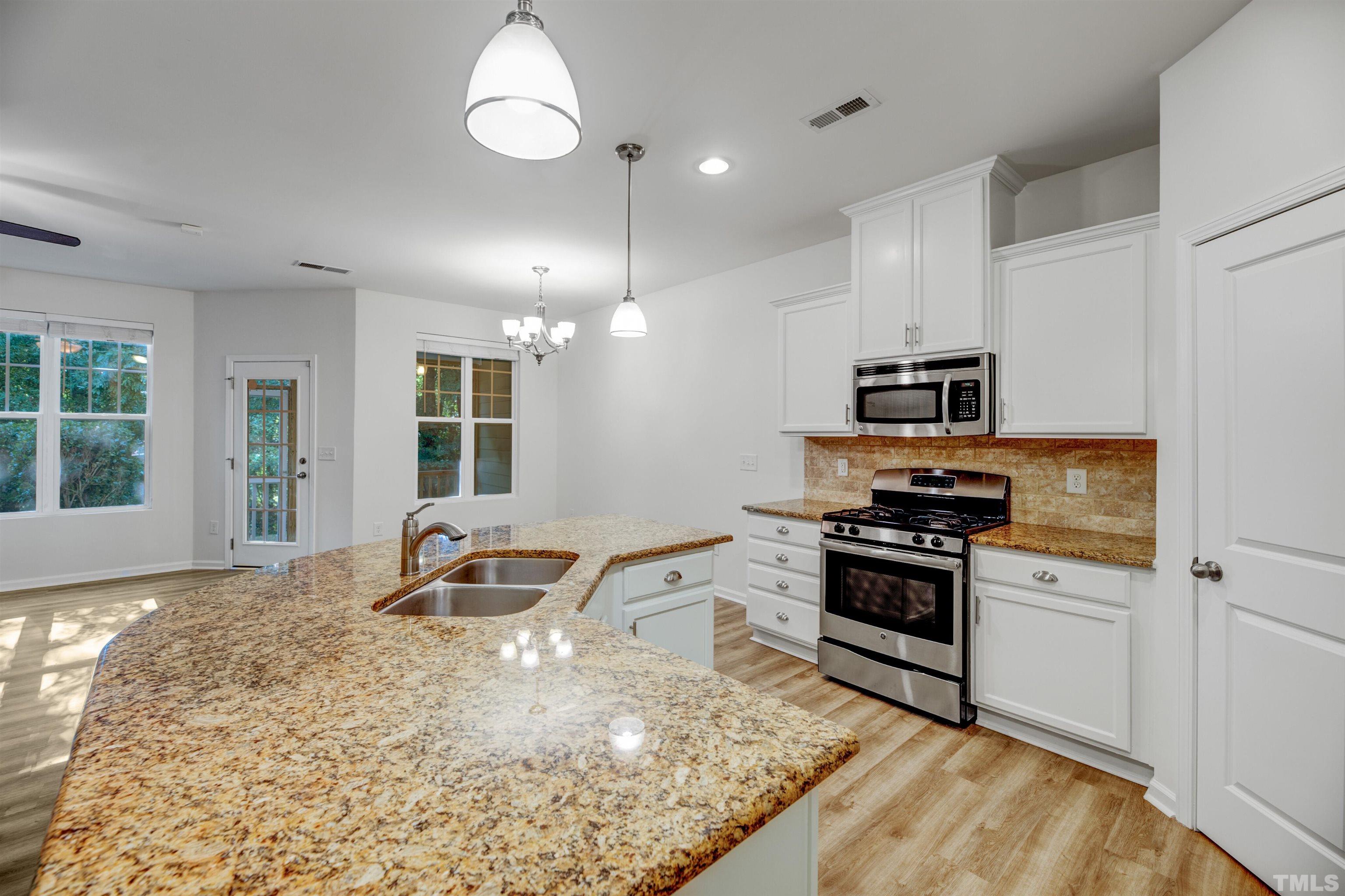 714 Treviso Lane Apex, NC 27502 - Photo 13 of 41 a kitchen with stainless steel appliances granite countertop a stove top oven a sink a dining table and chairs with wooden floor