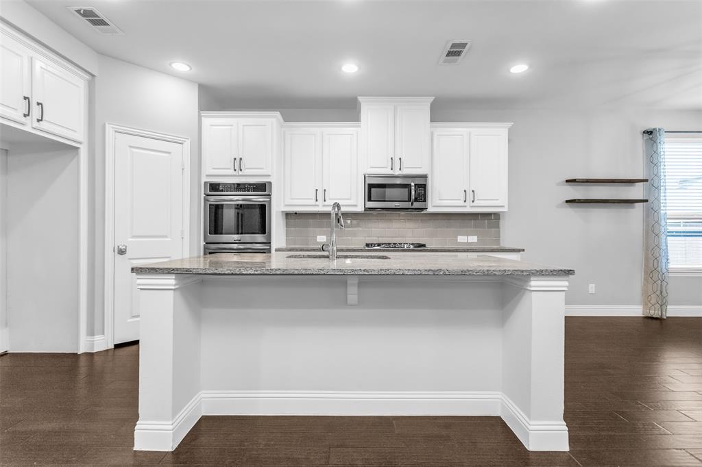 15713 Canyon Ridge Prosper, TX 75078 - Photo 27 of 38 Modern kitchen featuring a central island with a light-toned countertop, white cabinetry with dark hardware, stainless steel appliances, a subway tile backsplash, and dark wood-finish flooring