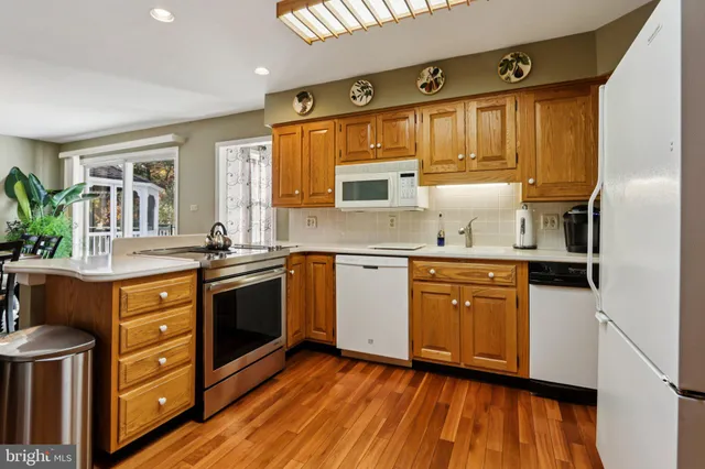 a kitchen with stainless steel appliances granite countertop wooden cabinets a refrigerator a sink a stove and wooden floors