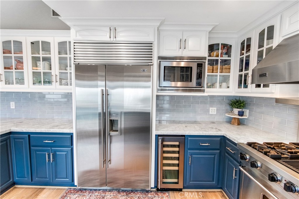 5522 Mossvale Circle Huntington Beach, CA 92649 - Photo 11 of 61 Luxury kitchen featuring waterfall marble, custom navy cabinetry, farmhouse sink, high-end appliances, and backyard views.