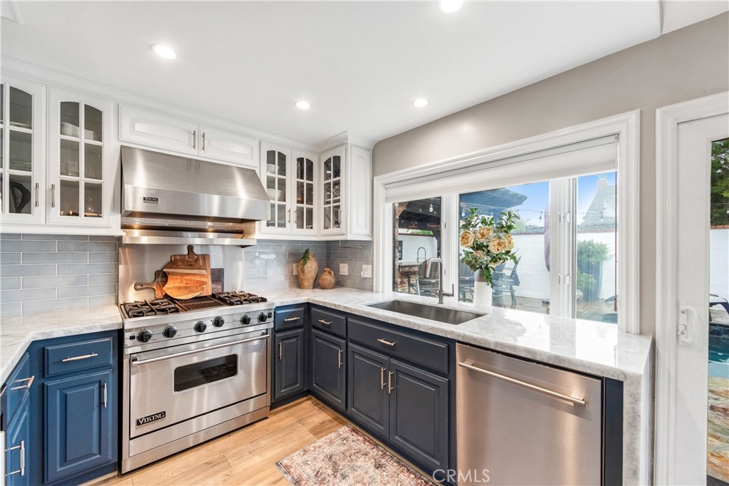 5522 Mossvale Circle Huntington Beach, CA 92649 - Photo 12 of 61 Luxury kitchen featuring waterfall marble, custom navy cabinetry, farmhouse sink, high-end appliances, and backyard views.