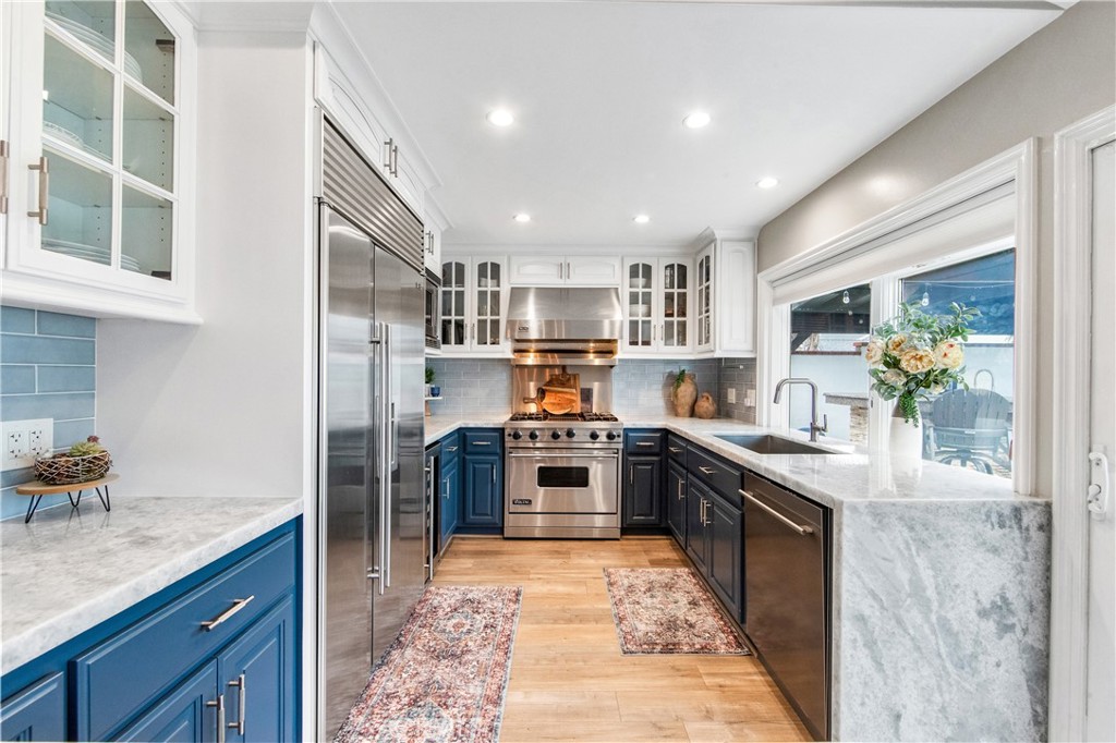 5522 Mossvale Circle Huntington Beach, CA 92649 - Photo 13 of 61 Luxury kitchen featuring waterfall marble, custom navy cabinetry, farmhouse sink, high-end appliances, and backyard views.