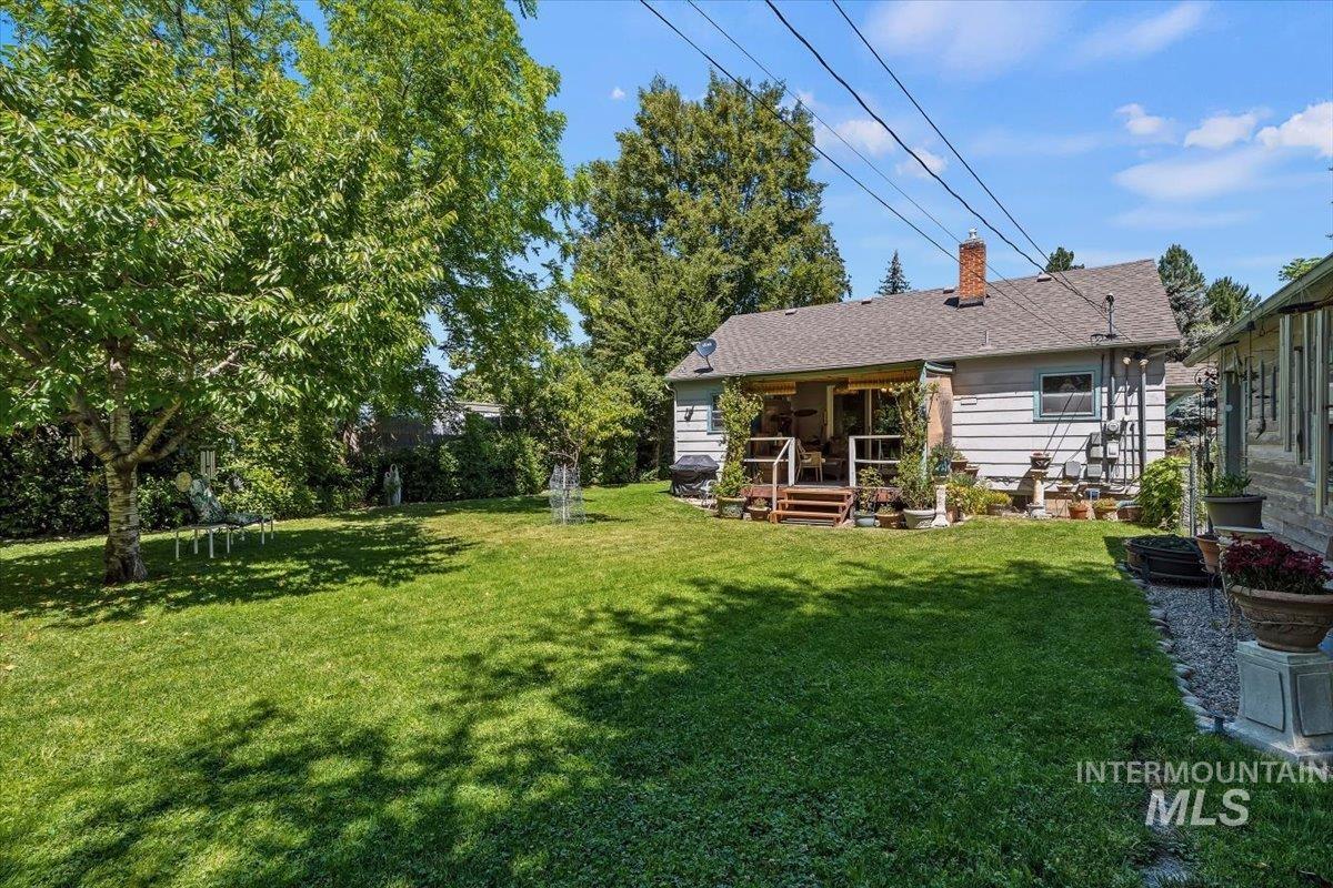 4619 Freemont Street Boise, ID 83706 - Photo 19 of 27 Expansive backyard featuring a manicured lawn, mature trees, a covered patio with wood decking, and a brick chimney