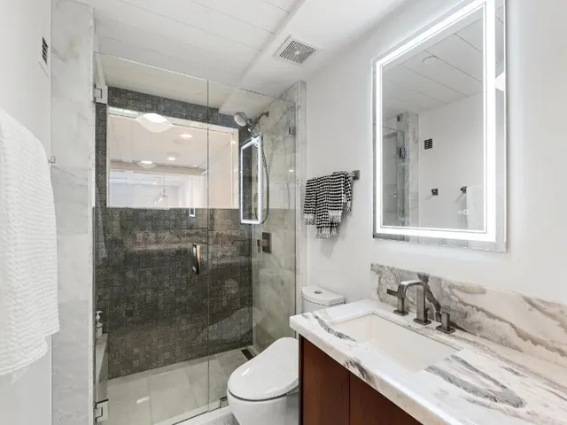a bathroom with a granite countertop sink a toilet a mirror and shower